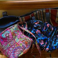All four bags grouped: floral quilted tote, black vented duffel, navy carryall with striped lining, abstract-pattern backpack