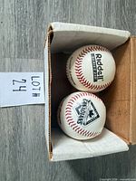 Two baseballs inside open box showing top panels and red stitching