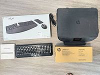 Overview of lot showing HP Envy 5540 printer, boxed Microsoft Sculpt Desktop set, HP toner cartridge, Apple SuperDrive box, and additional keyboard.