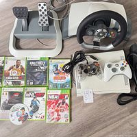 Overall bundle showing console, controllers, steering wheel, pedals, nine games and cables