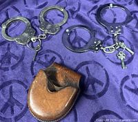 Two pairs of handcuffs with keys and leather pouch on purple fabric