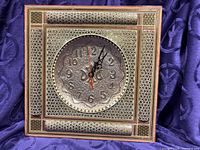 Front view of square gold-tone wall clock with ornate pattern
