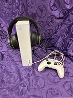 Console standing vertically with headset on top, controller and cords visible