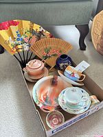 Overall view of assorted porcelain items and fans in box
