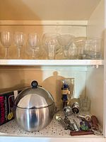 Cabinet shelves with assorted bar glasses, ice bucket, boxed kits, wine tools