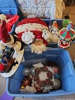 Overview of tote with Christmas decorations including snowman on sled, tinsel wreath, Santa head, carousel, stained glass wreath and assorted ornament balls