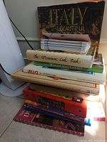 Stack of assorted cookbooks showing Italy The Beautiful Cookbook, The Uncommon Cookbook, Woodfield Cooks, Jell-O book and others