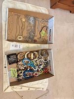 Full lot showing two MaxSold trays filled with costume jewellery and cream hanging organizer