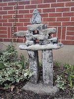 Full view of Inukshuk against brick wall and plants