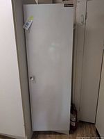 Full view of white metal cabinet standing between other cabinets, door closed