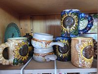 Shelf with sunflower mugs, soup crocks, potpourri pot, decorative plate and additional mugs