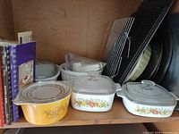 Shelf view showing Pyrex casserole, CorningWare casseroles, pizza pans, cooling rack, cookbooks