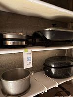 Shelf with Rival electric skillet, waffle maker, enamel roaster and cast aluminum pot