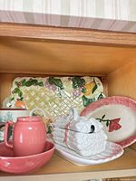 Group view of ceramic platter, covered dish, teapot, creamer and tray on shelf