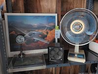 Shelf displaying wall art poster, desk fan, heater, desk clock
