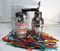 Both cocktail shakers upright, corkscrew on top, pile of swizzle sticks