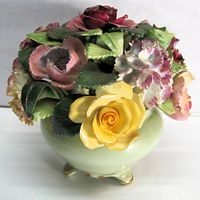 Angled view of green footed vase with multicolor bone china flowers
