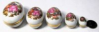 Five closed egg trinket boxes lined smallest to largest beside a coin for scale