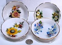 Front view of all four bowls showing floral designs and scale with coin