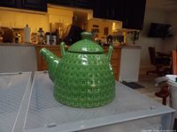 green ceramic teapot showing shape, lid, spout, handle, surface pattern