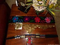 Overview of three belts on table: embroidered floral belt, gold coin hip scarf, beaded coin belt