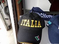 Black Italia cap with yellow lettering and flag patch; partial view of additional caps