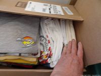 Open box showing stacked graphic t-shirts, grey Hard Rock Cafe logo visible