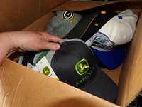 Box containing John Deere, Green Bay Packers and white-blue-green caps