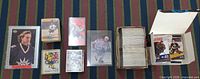 Overview of oversized card, snap cases, rigid holders and long box of cards with sealed packs visible