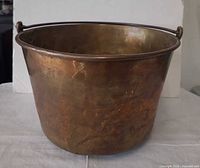Side view of brass pot showing exterior patina, dents, bail handle
