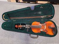 Violin inside open hard case with bow, showing interior padding and accessories