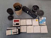 Group shot of three lenses, filter boxes, lens hood, caps, paperwork