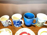 Four mugs with assorted patterns and partial view of saucers