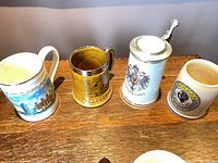 Four rear mugs: scenic landmark mug, gold relief mug, lidded German stein, Nürnberg crest mug