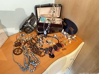 Lot overview showing jewelry pieces spread on dresser, jewelry box open, and two masquerade masks