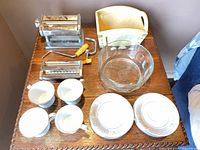 Top view of all items arranged on wooden table: pasta maker, glass bowl, napkin holder, teacups, saucers
