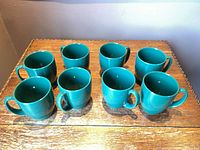Eight matching green mugs on wooden surface
