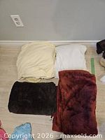 Four folded linens: two fitted sheets (yellow, white), two fleece blankets (brown, rust)