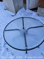 Top view of round glass patio table showing umbrella hole and snow cover