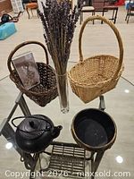 Overall view of items on glass table: two baskets, vase with lavender, cast iron teapot, decorative bowl