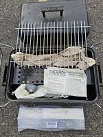 Open grill showing grate, burner pan, regulator, instruction sheet
