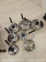 Eight stainless pots and saucepans with lids displayed on floor