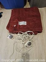 Rust red electric blanket folded with controllers and cords visible