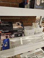 Shelf showing boxed Black+Decker SteamWorks steamer, Flags Unlimited package, clear plastic diffuser, bins with bolts