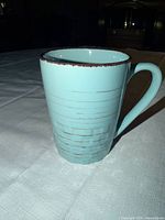 Full view of blue ceramic mug with distressed brown rim and weave pattern