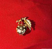 Front view of gold-tone apple brooch with diamonds displayed on red background