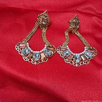 Front view of both gold-tone crystal drop earrings on red fabric