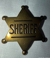 Front view of goldtone six-point sheriff star badge with raised lettering