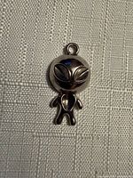 Front view of silver-tone alien pendant on textured background