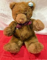 Full view of brown Gund teddy bear seated on red surface